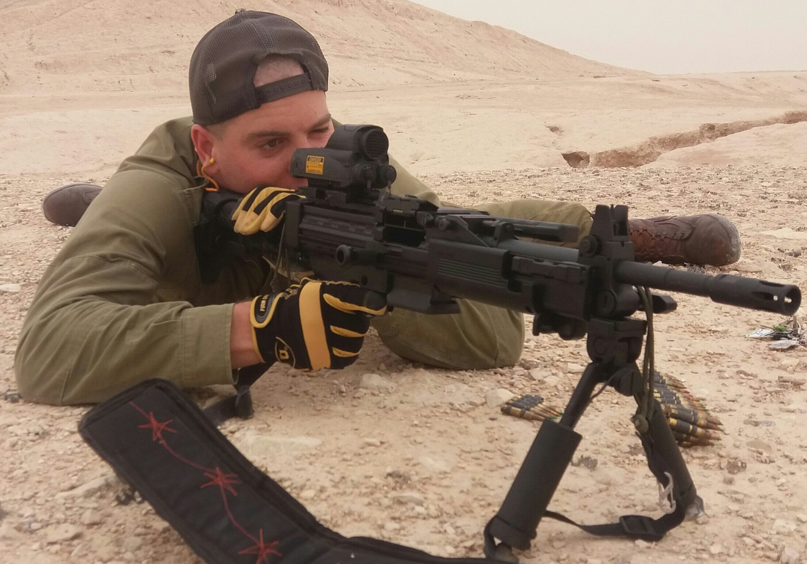 Instrutor em posição de tiro com armamento em terreno desértico
